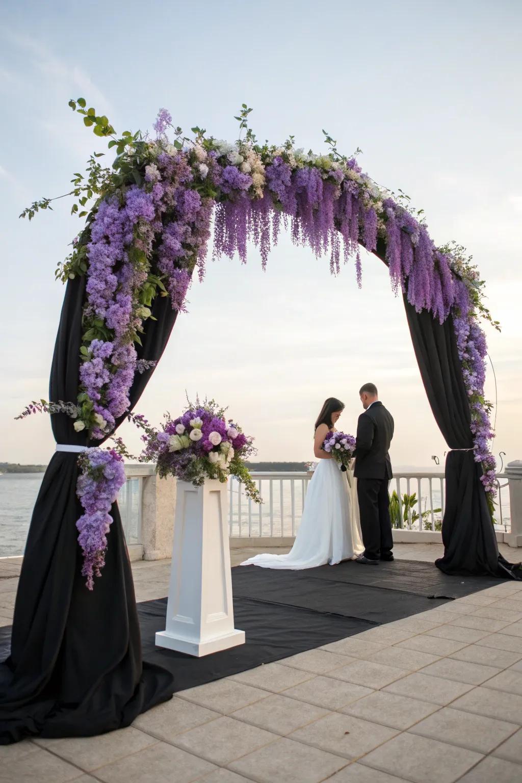 A charming ceremony arch decorated with violet wisteria and dark fabric.