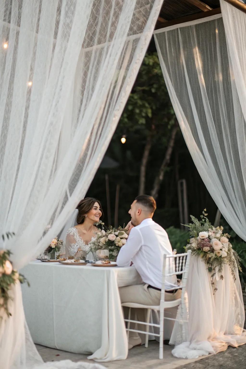 A bride and groom table surrounded by sheer drapery for a dreamy effect.
