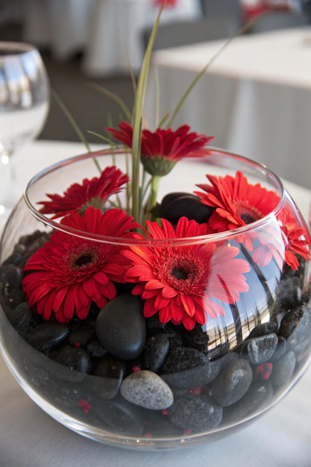 Suspended scarlet blooms above jet-black stones inside a see-through bowl, crafting a serene ornamental display.