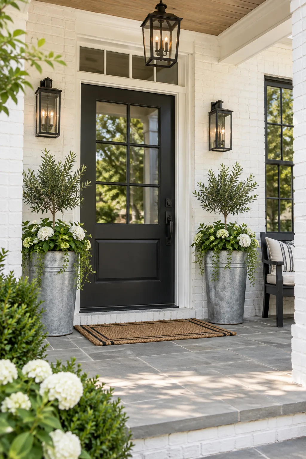 A modern farmhouse front porch with a matte black door and galvanized planters against white brick.