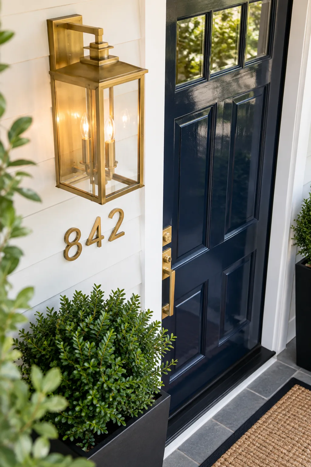 An oversized brass wall lantern glowing warmly next to the top corner of a navy blue front door.