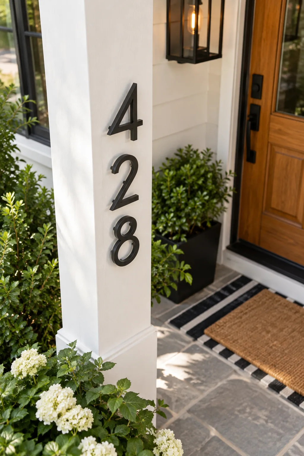 Modern black metal house numbers floating slightly off a white porch column.