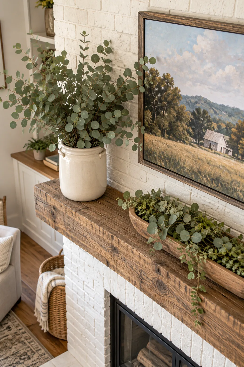 Left side of a wood mantel with a white ceramic crock holding tall green eucalyptus branches that reach the middle of the TV screen.