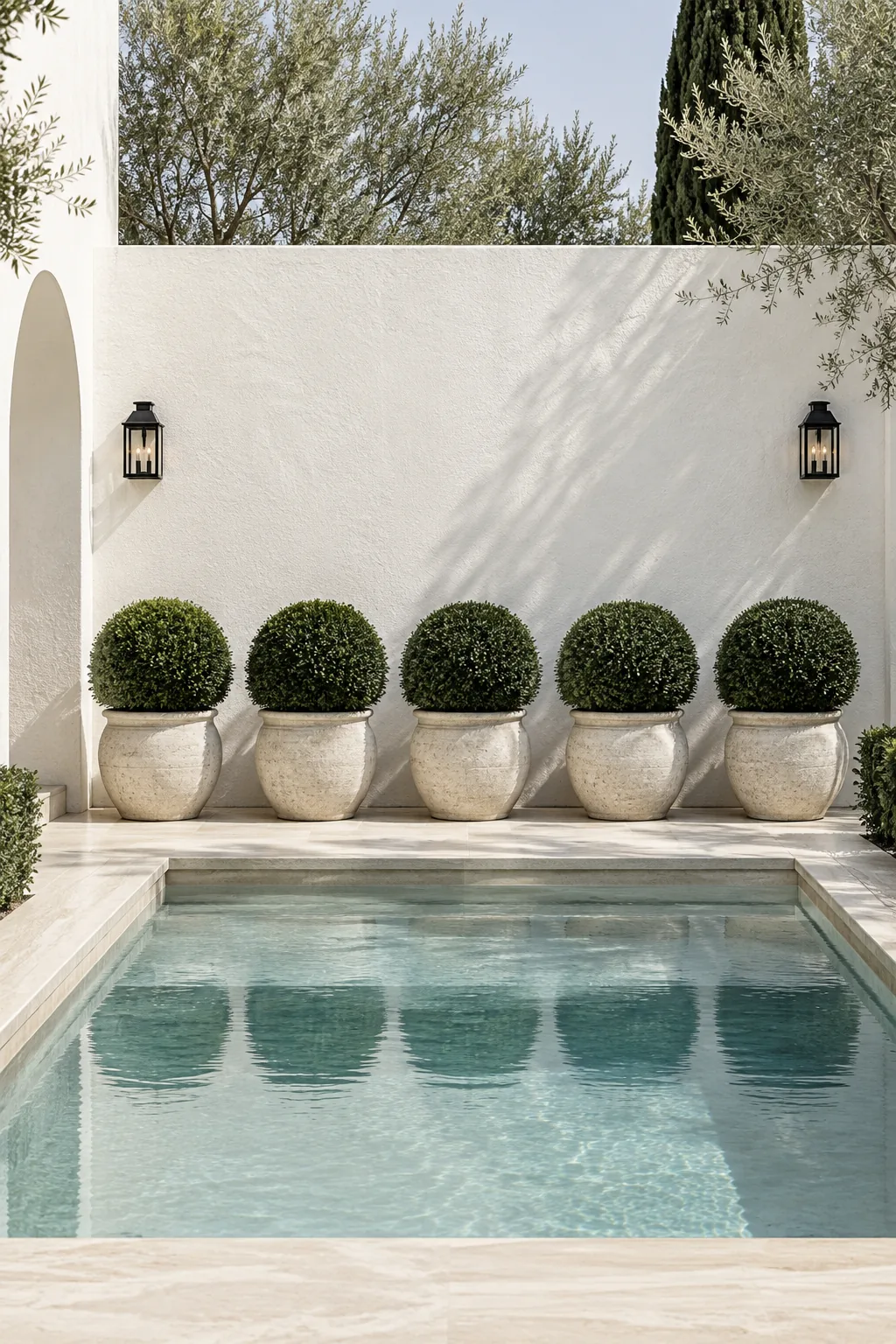 A perfectly straight row of trimmed boxwood shrubs against a white wall near a pool