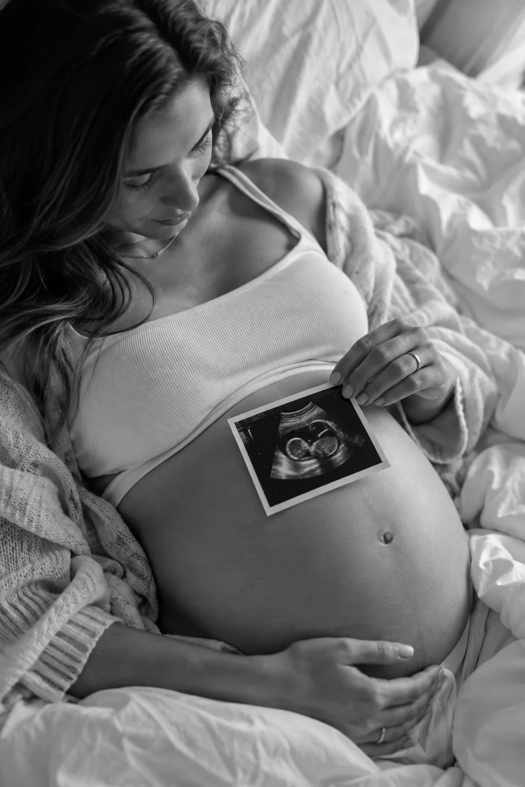 Pregnant woman lying on bed holding an ultrasound photo
