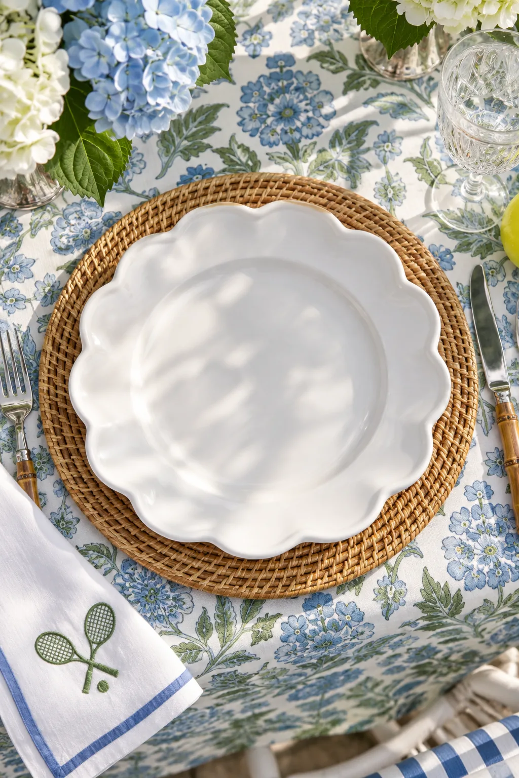 Close-up of a woven rattan charger plate layered between a floral tablecloth and a white dinner plate.