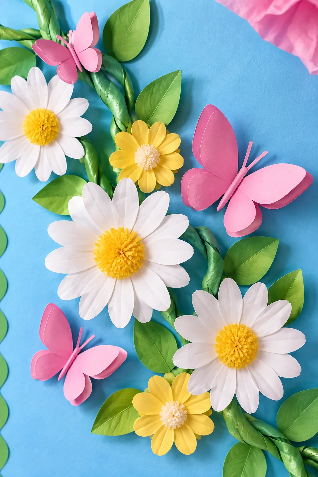 Small white paper daisies and folded pink butterflies arranged along a green paper vine.