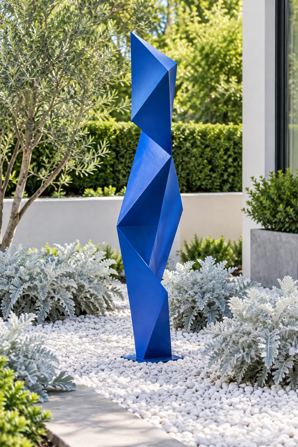 Tall blue geometric metal sculpture in a modern gravel garden with silver foliage.
