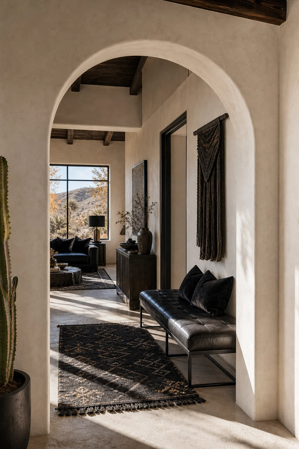 View from the living room into a connecting hallway, where a bone-white adobe archway frames a sleek, tailored black leather bench.